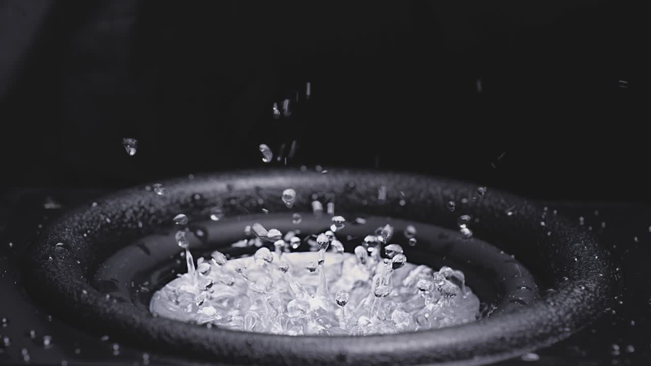 Dark Wave Audio and Black Water Liquid on a Plate. Subwoofer speaker with water. Droplets explode over the sound of the bass. Liquid jumps on the audio speaker. Background for a party. Slow motion.