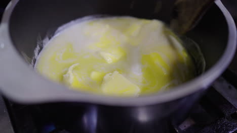 cubes of butter melt in a black saucepan over a flame as the first step of preparing bagna cauda, a traditional piedmontese sauce made with garlic, anchovies, and olive oil, gently stirred by hand.