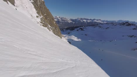 Epic-FPV-dive-down-a-huge-mountain-and-race-next-to-a-ski-slope-in-winter-resort