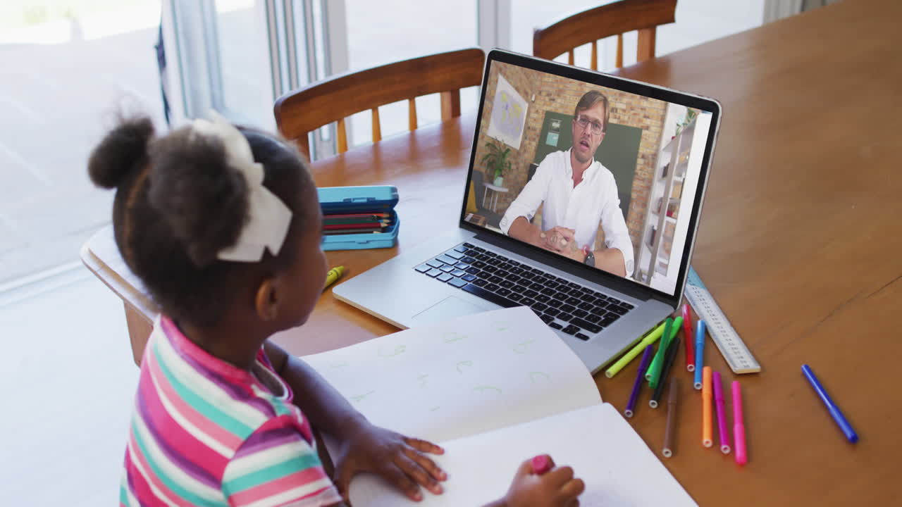 African american girl doing homework while having a video call with male teacher on laptop at home