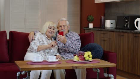 Grandmother-and-grandfather-making-video-call-online-on-mobile-phone-at-home.-Smiling-senior-couple