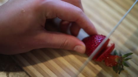 toma en cámara lenta de alguien que usa un cuchillo afilado para cortar algunas fresas rojas y frescas