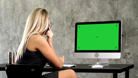 beautiful young businesswoman working on computer and making a call. green screen mock-up display