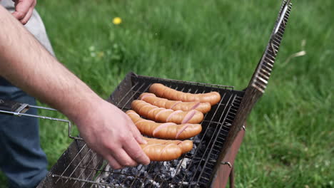 man prepares juicy sausages in barbecue on picnic. cook putting sausages into a grill for frying. fried sausages are cooking on coals in the garden.