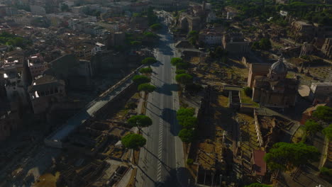 Vista-De-ángulo-Alto-De-La-Carretera-En-La-Ciudad-Rodeada-De-Restos-De-Sitios-Antiguos.-Incline-Hacia-Arriba-La-Revelación-Del-Paisaje-Urbano-Con-El-Anfiteatro-Del-Coliseo-En-La-Distancia.-Roma,-Italia