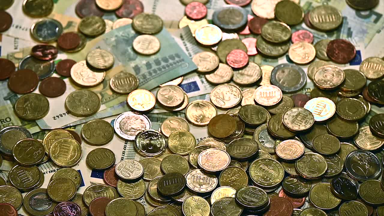 una avalancha de monedas de euro vertidas en una pila de cinco billetes de euro sobre una mesa, ángulo de cierre
