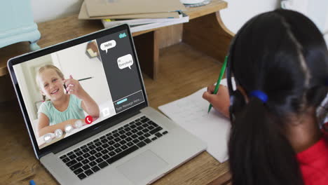 schoolgirl using laptop for online lesson at home, with girl talking and web chat on screen