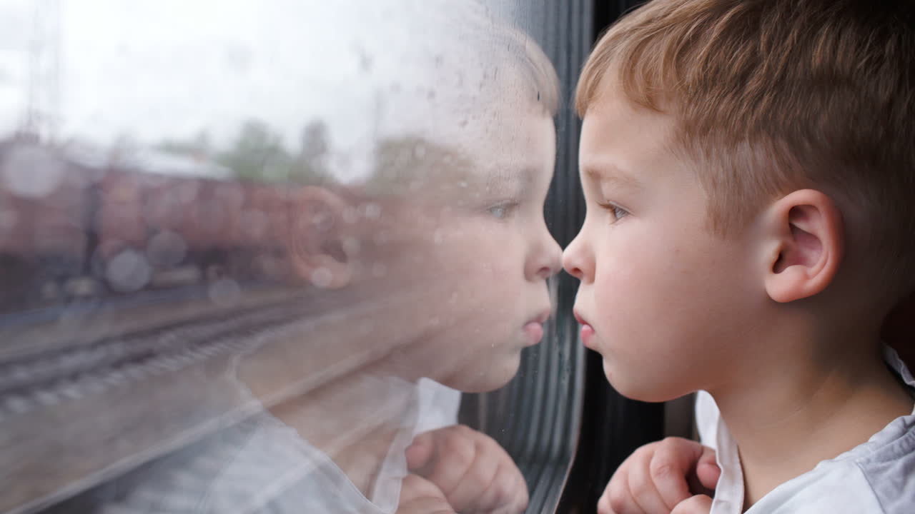 Curious boy looking out of the train window in rainy weather