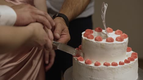 hands cutting a white two-tiered cake with orange frosting, symbolising a joyous celebration event