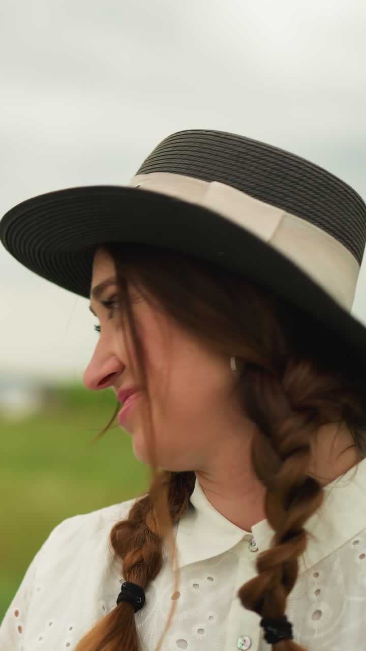 un primer plano de una mujer con un vestido blanco y un sombrero de borde ancho, sonriendo tímidamente mientras mira hacia el lado. un hombre en el fondo, con una camisa a cuadros, señala una dirección