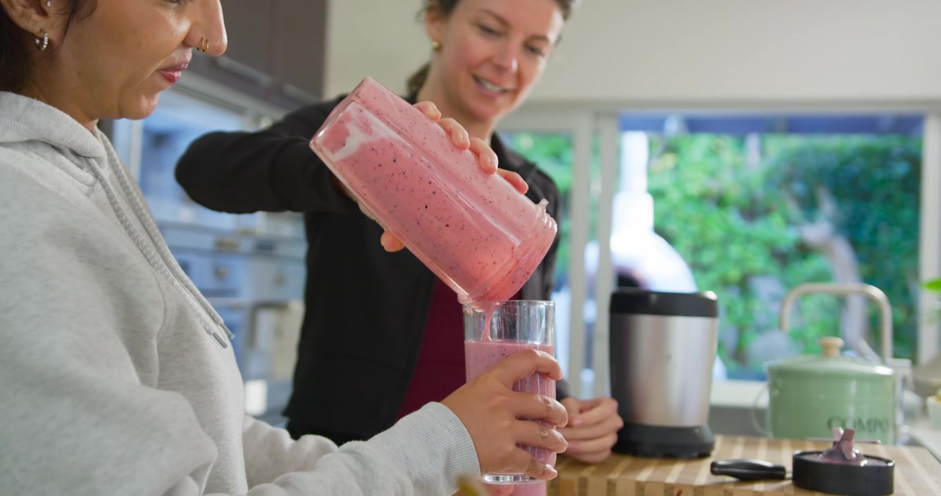 Donne di diverse etnie che versano, una donna inclina una brocca e serve un frullato rosa in un bicchiere al bancone