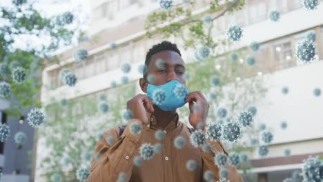 Multiple-covid-19-cells-floating-against-african-american-man-wearing-face-mask-on-the-street