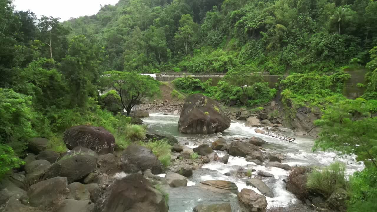 Aerial view of a rocky Philippine river winding through dense tropical forest, with whitewater rapids and a hillside road blending rugged terrain and vibrant greenery