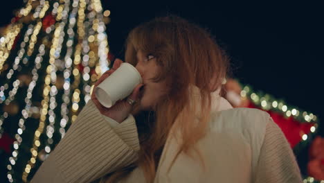 una chica bebiendo café, luces de árbol de navidad en el fondo, primer plano. una mujer bebiendo.