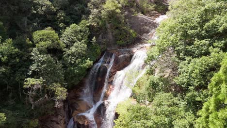 a beautiful aerial shot pushing in on a powerful waterfall. the water cascades over large rocks, surrounded by a lush, green forest in a remote japanese mountain landscape.