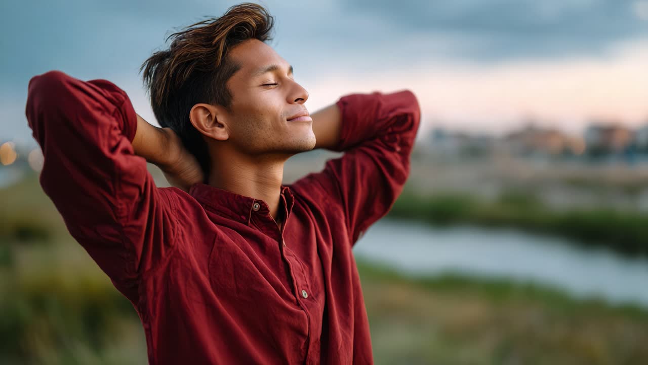 A young man in a red shirt enjoys a serene moment in nature, basking in the calmness of the environment while feeling the gentle breeze on his face