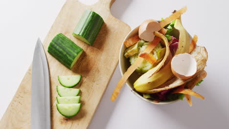 video aéreo de cuchillo y pepino en la tabla de cortar, con residuos orgánicos en el contenedor de compostaje de la cocina