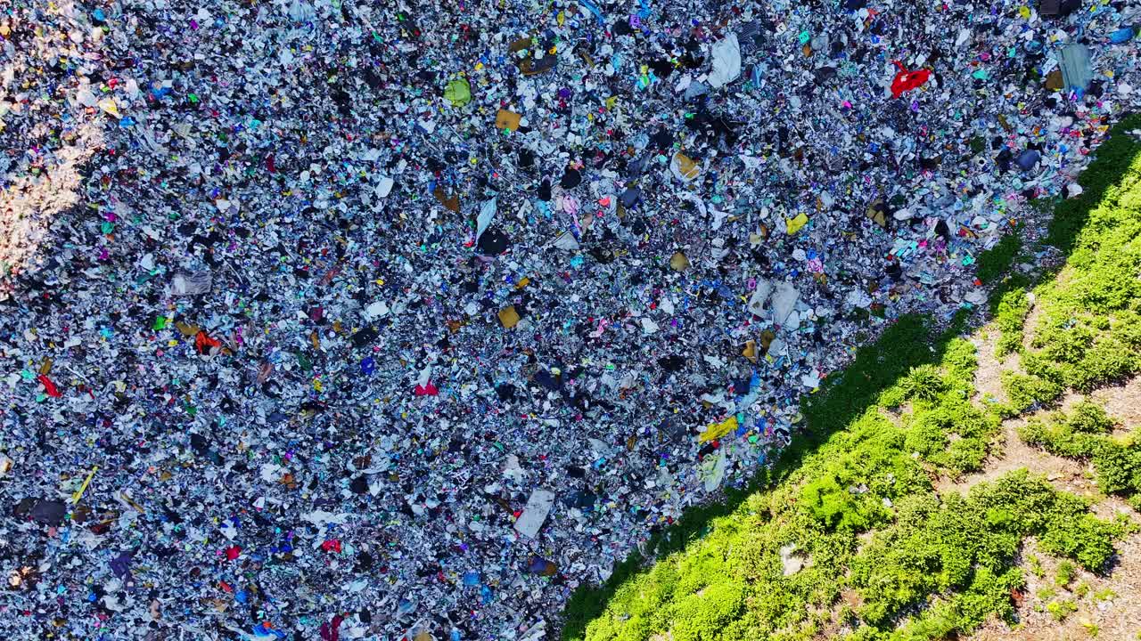 Vista aerea dall'alto che mostra il bordo della discarica che incontra piante verdi vivaci sottostanti.