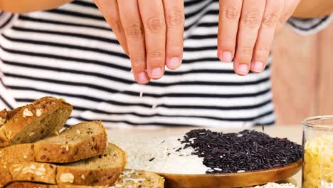 hands organize various grains and bread slices on a wooden board in a well-lit kitchen setting