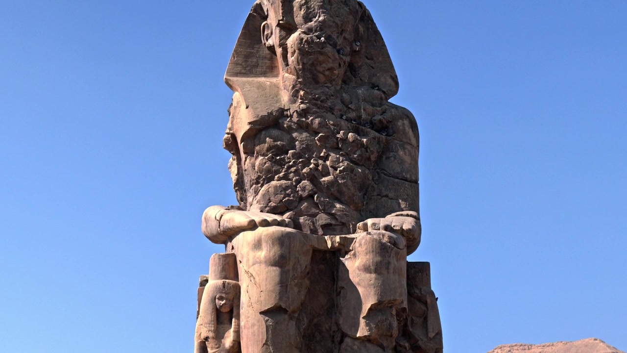 Una toma media, en contrapicado, centrándose completamente en la mitad superior erosionada de uno de los Colosos de Memnón en Luxor, Egipto