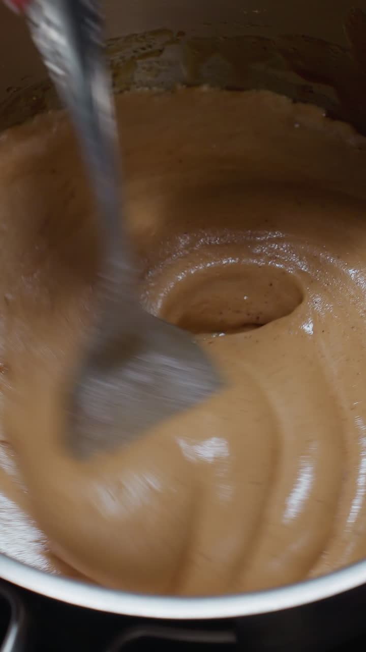 Close-up of cook stirring smooth pap on electric stove, creating a creamy texture with a partial view of a white plate, the thick porridge swirls as it is carefully prepared