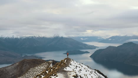 hiker at the end of a ridge line atop roys peak in new zealand taking photos and looking at view