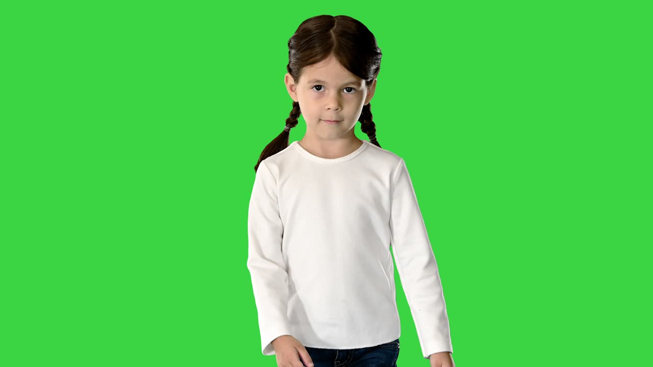 niña con cola de cerdo vestida con una camiseta blanca de manga larga y vaqueros caminando y mirando a la cámara en una pantalla verde, llave cromada