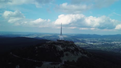 jested tower during a part clouded day with liberec town in the distance, drone fly away, 4k or uhd, 30fps