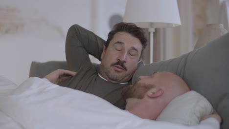 happy homosexual men lying in bed in morning and talking