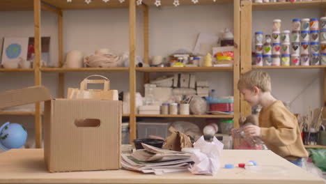 little blonde girl and blond kid picking up craft supplies on a table in a workshop