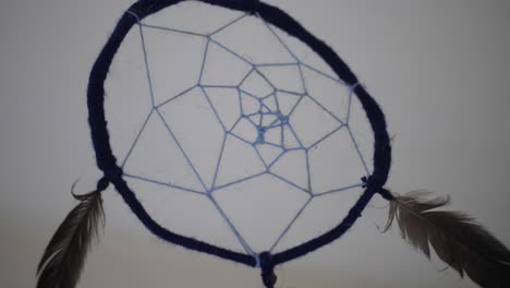 a close up of a dreamcatcher with feathers inside a dark, abandoned room with a simple white backgorund and ceiling