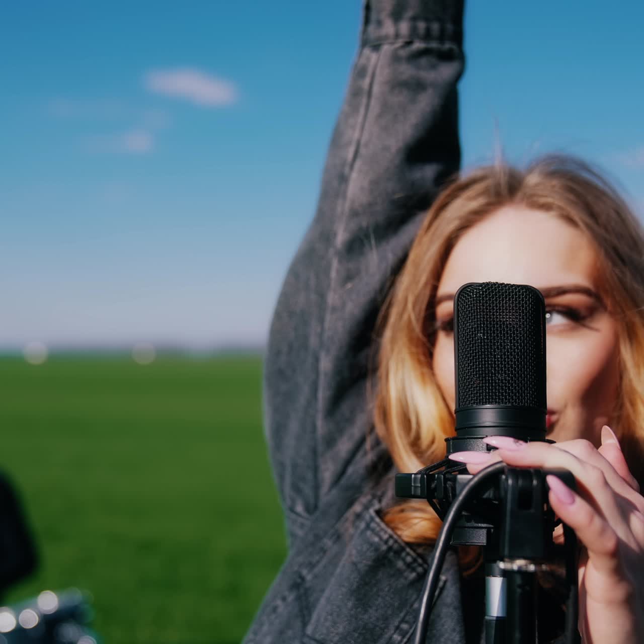 Young woman singer performing music outdoors. Beautiful female soloist singing into a microphone on nature background