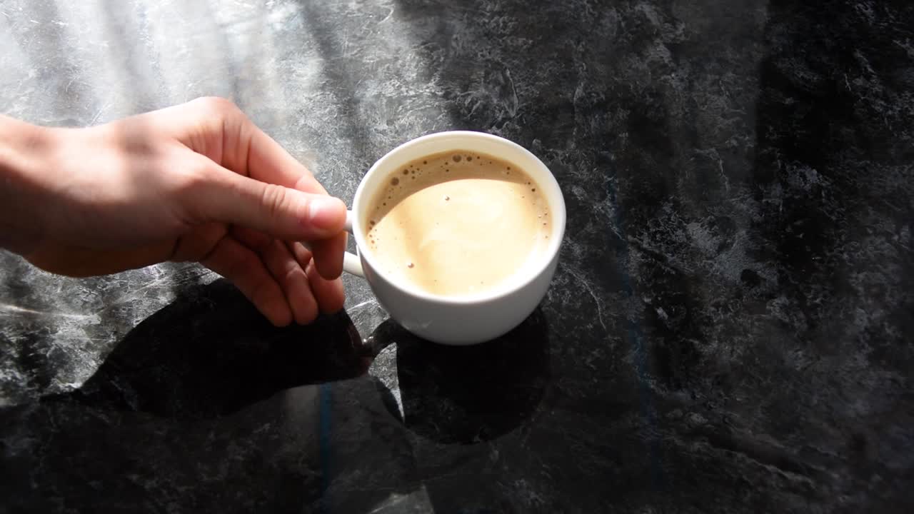 Placing a white freshly made cup of coffee onto a black marbled table top