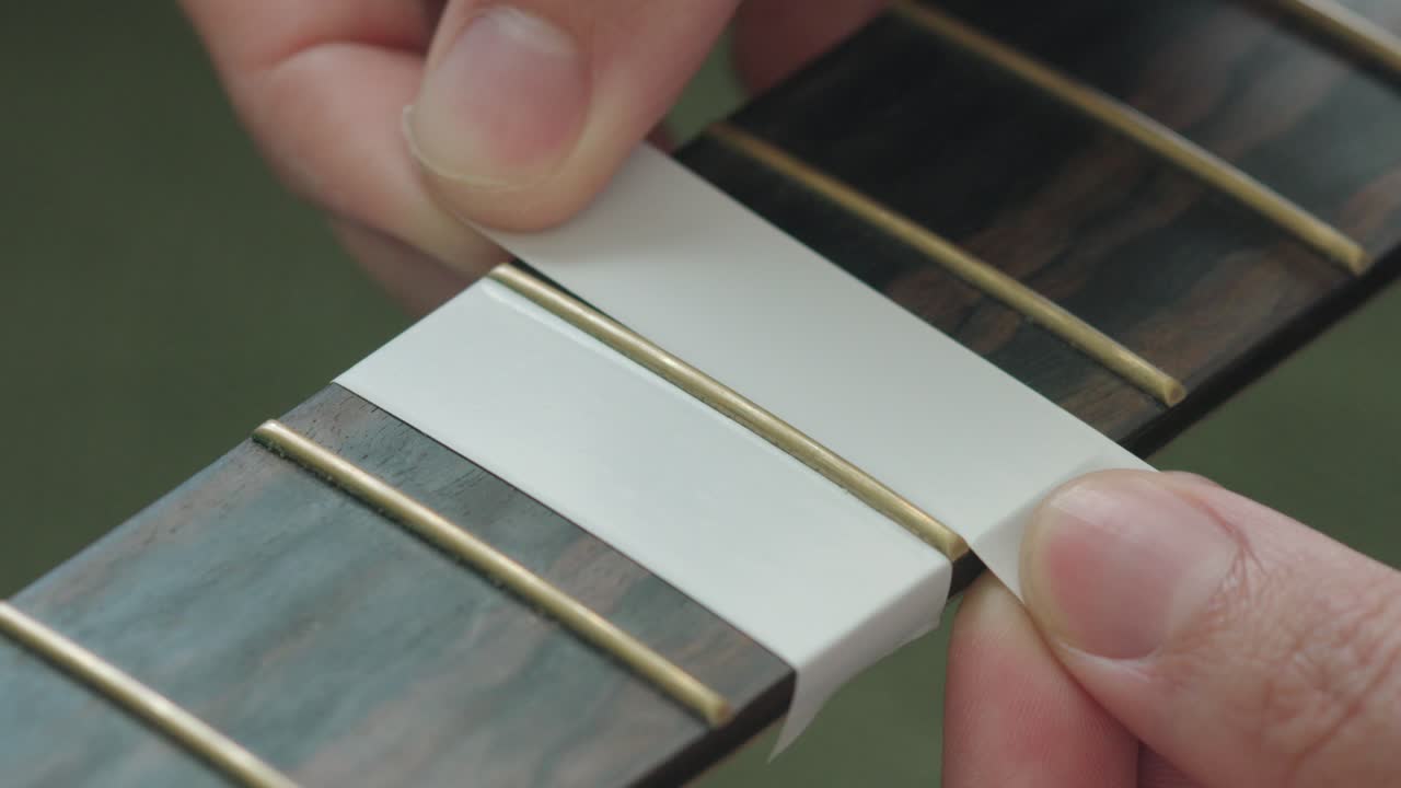Man Putting Masking Tape On The Fingerboard Of An Acoustic Guitar To Protect Before Polishing The Frets
