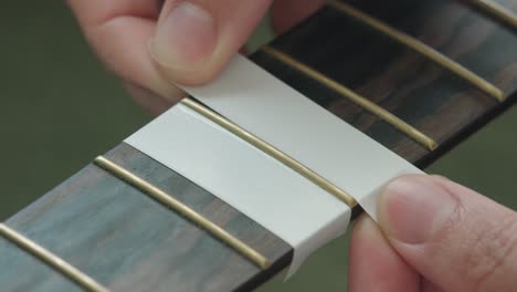 hombre poniendo cinta adhesiva en el diapasón de una guitarra acústica para protegerla antes de pulir los trastes