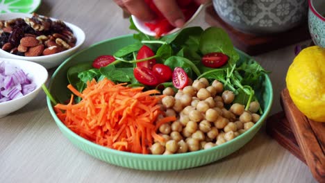 wide shot making of a salad adding tomatoes carrots spinach chick peas lemons onions nuts dressing in view