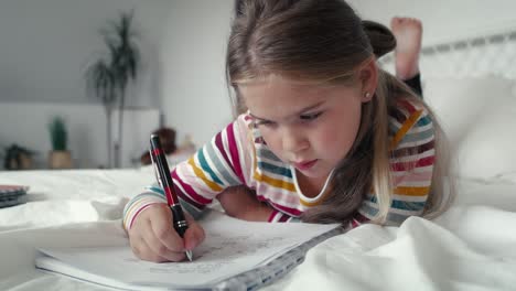 Elementary-age-girl-studying-while-lying-on-front-on-the-bed