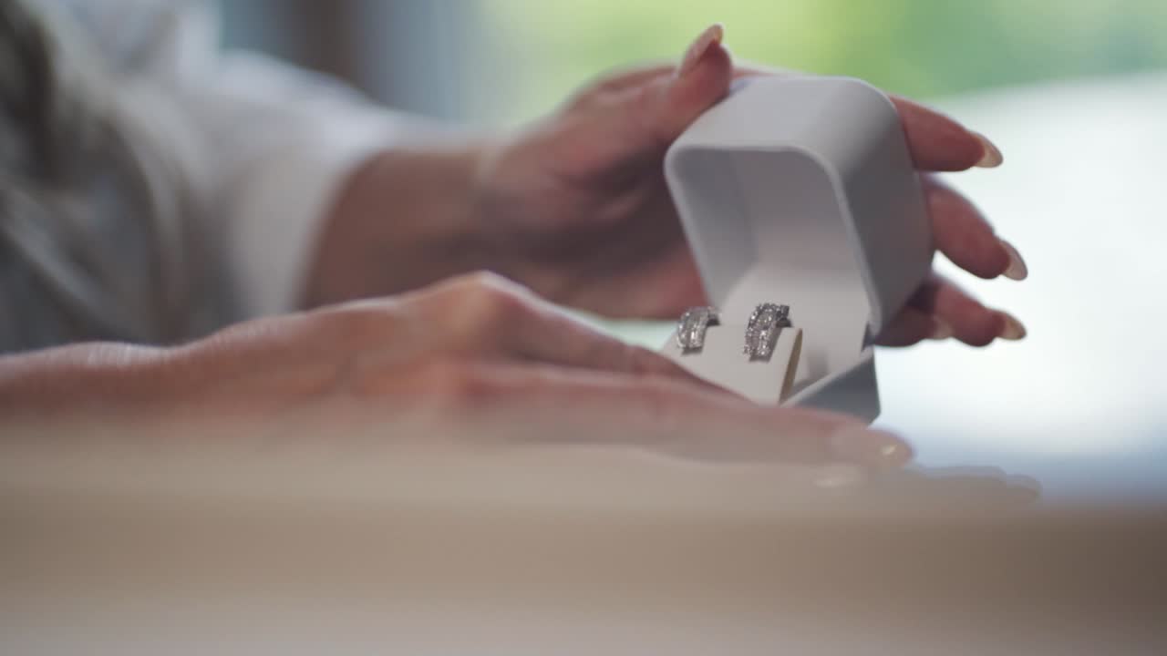A woman holds and opens a white box with two diamond earrings inside