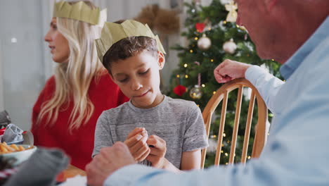 son playing with christmas cracker novelty gift sitting at dinner table with mother and grandfather