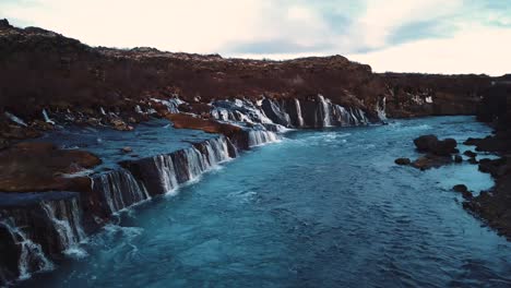 drone with cinematic movements shows beautiful icelandic waterfall, hraunfossar, in sunset light from multiple angles