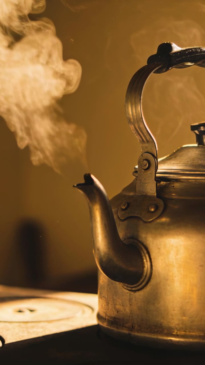 Vertical video: Burner heating vintage kettle, releasing thick steam over stovetop with amber light