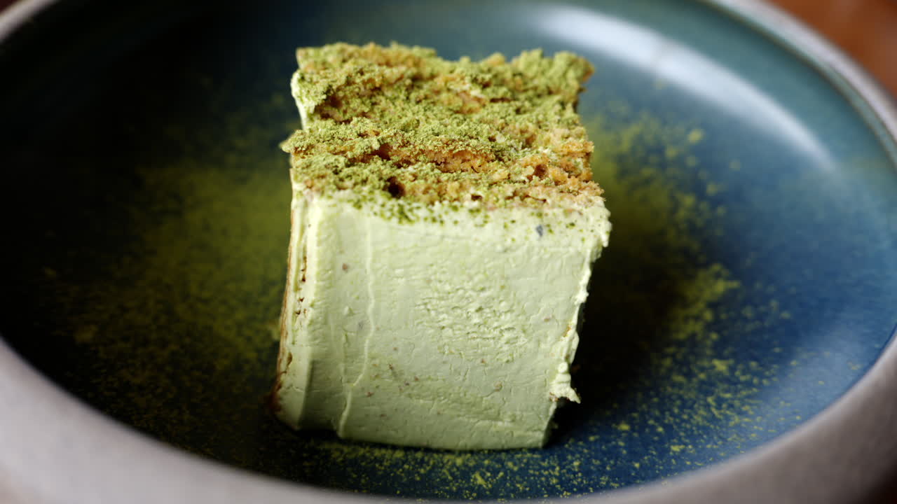 Close up of a piece of cake with matcha powder on a blue plate at a restaurant