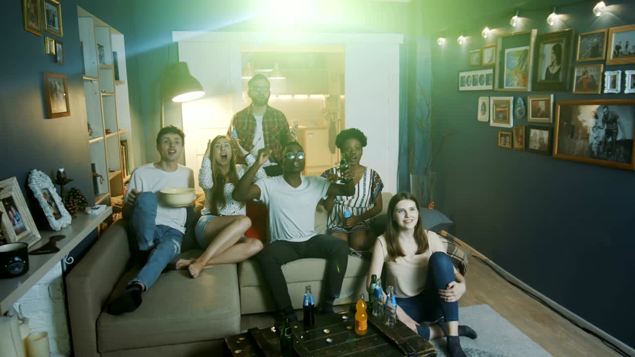 쾌활한 젊은 다민족 팬 친구들은 집에서 프로젝터로 tv에서 스포츠를보고, 팀을 지원하는 슬로우 모션을 외니다.