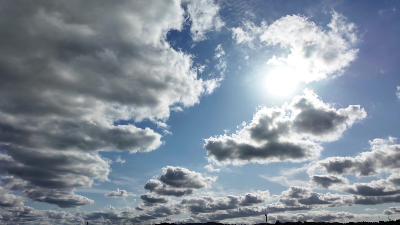 Bright Sun Shining Through Moving Clouds in Blue Sky
