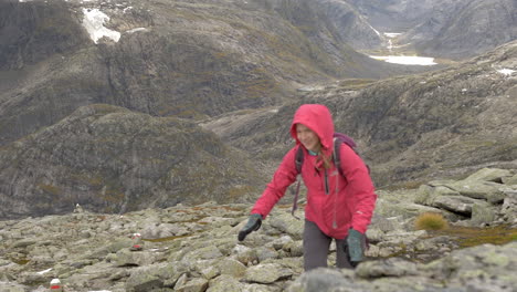 a woman smiles as she hikes up a steep rocky landscape on a cold, overcast day in norway