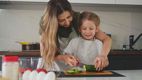 kid with mother in kitchen learns to cut green