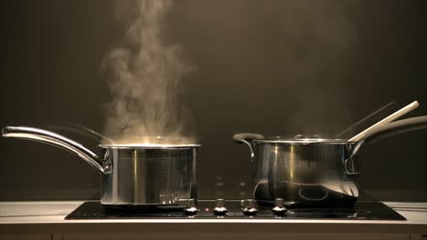 tight shot of a pair of simmering pans on a cook top with steam rising into a rangehood