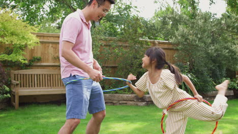 Asian-Father-And-Daughter-Having-Fun-Playing-With-Hula-Hoop-In-Garden-At-Home