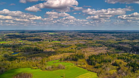Cloudscape over countryside farmland fields and forests in a green, rural landscape - aerial time lapse