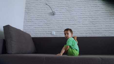 kid sitting on a big sofa switches on the light. baby boy playing with light at home.